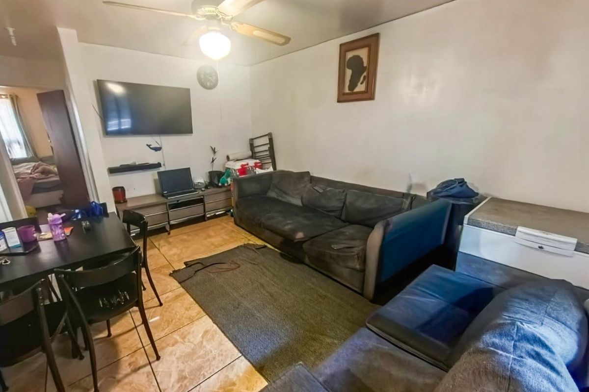 A living room area featuring tiled flooring and a ceiling fan, providing a functional space with potential for cosmetic updates.