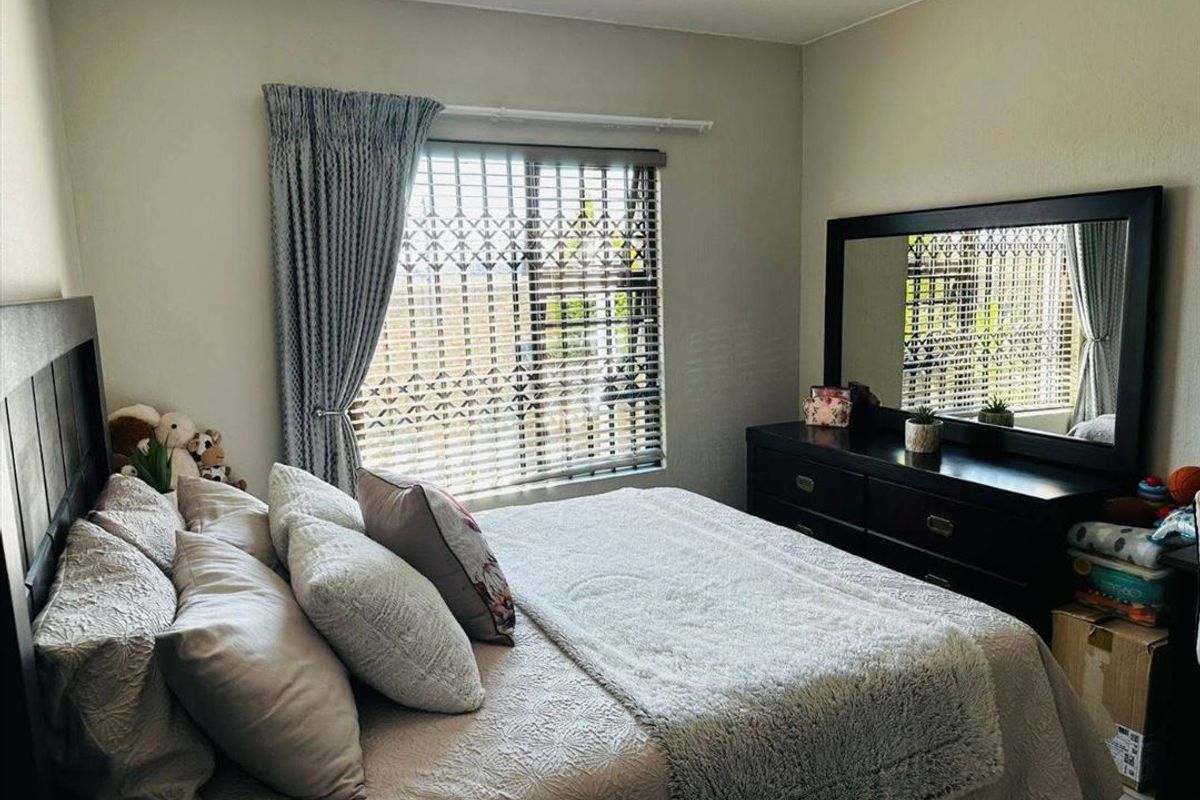 A well-lit bedroom featuring neutral wall tones, a window fitted with venetian blinds, and integrated curtain tracks.