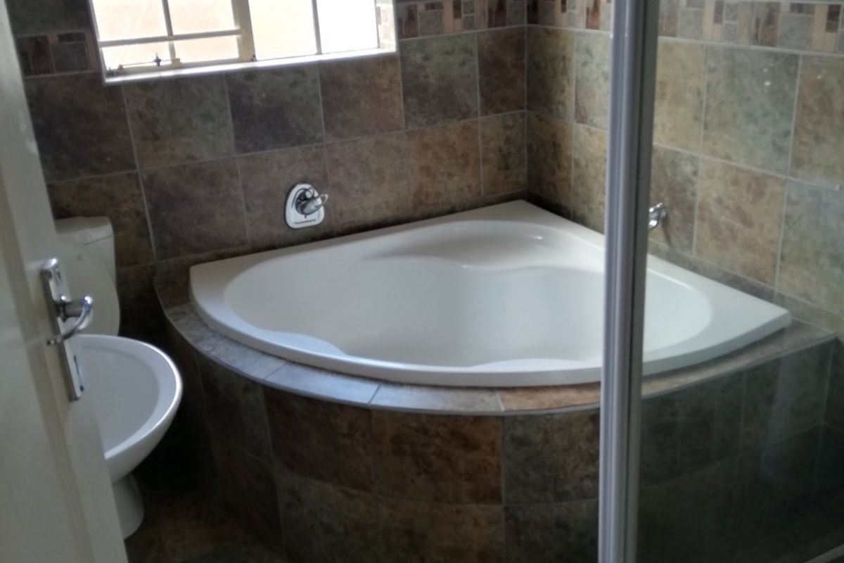 A functional bathroom featuring a corner bathtub, separate shower enclosure, and tiled finishes throughout.
