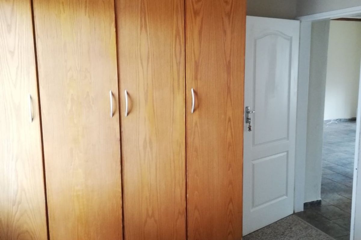 A bedroom featuring built-in wooden cupboards, carpeted flooring, and a ceiling fan, leading into an adjacent tiled room.
