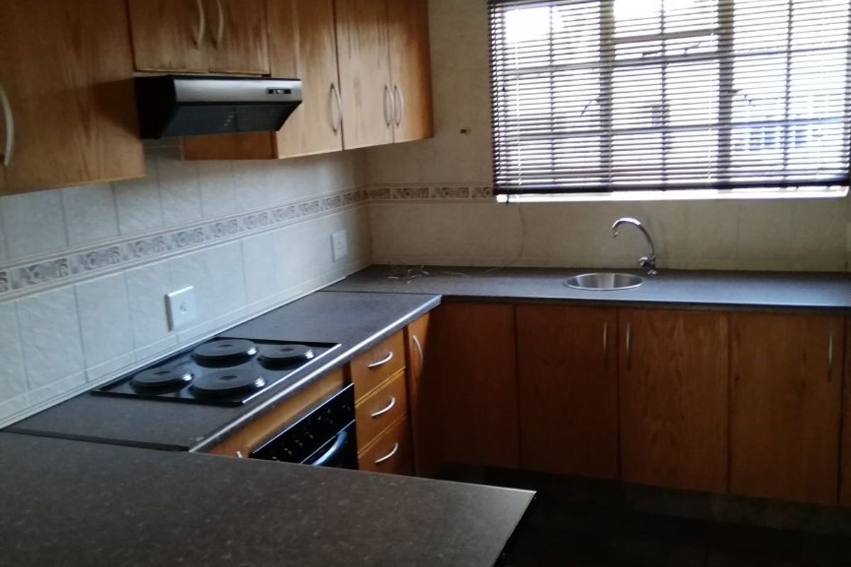 A functional kitchen featuring wooden cabinetry, dark laminate countertops, an integrated electric hob, oven, and a stainless steel sink with tiled finishes.