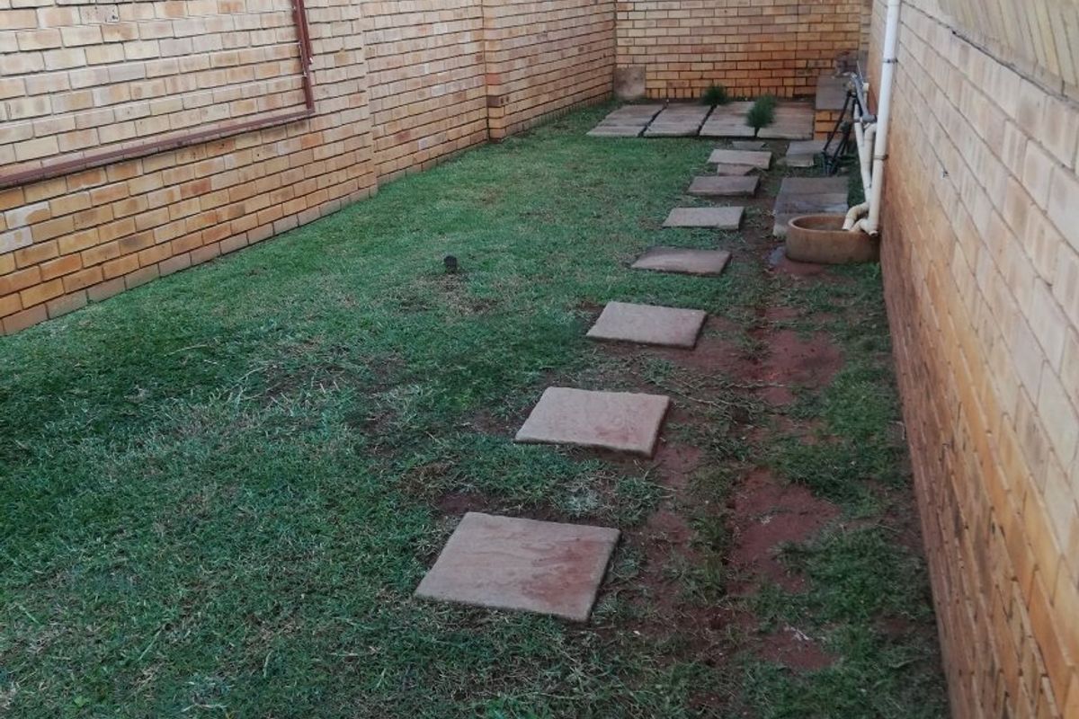 A private rear garden area featuring a face brick boundary wall, a built-in brick fireplace, and a paved walkway through the lawn.