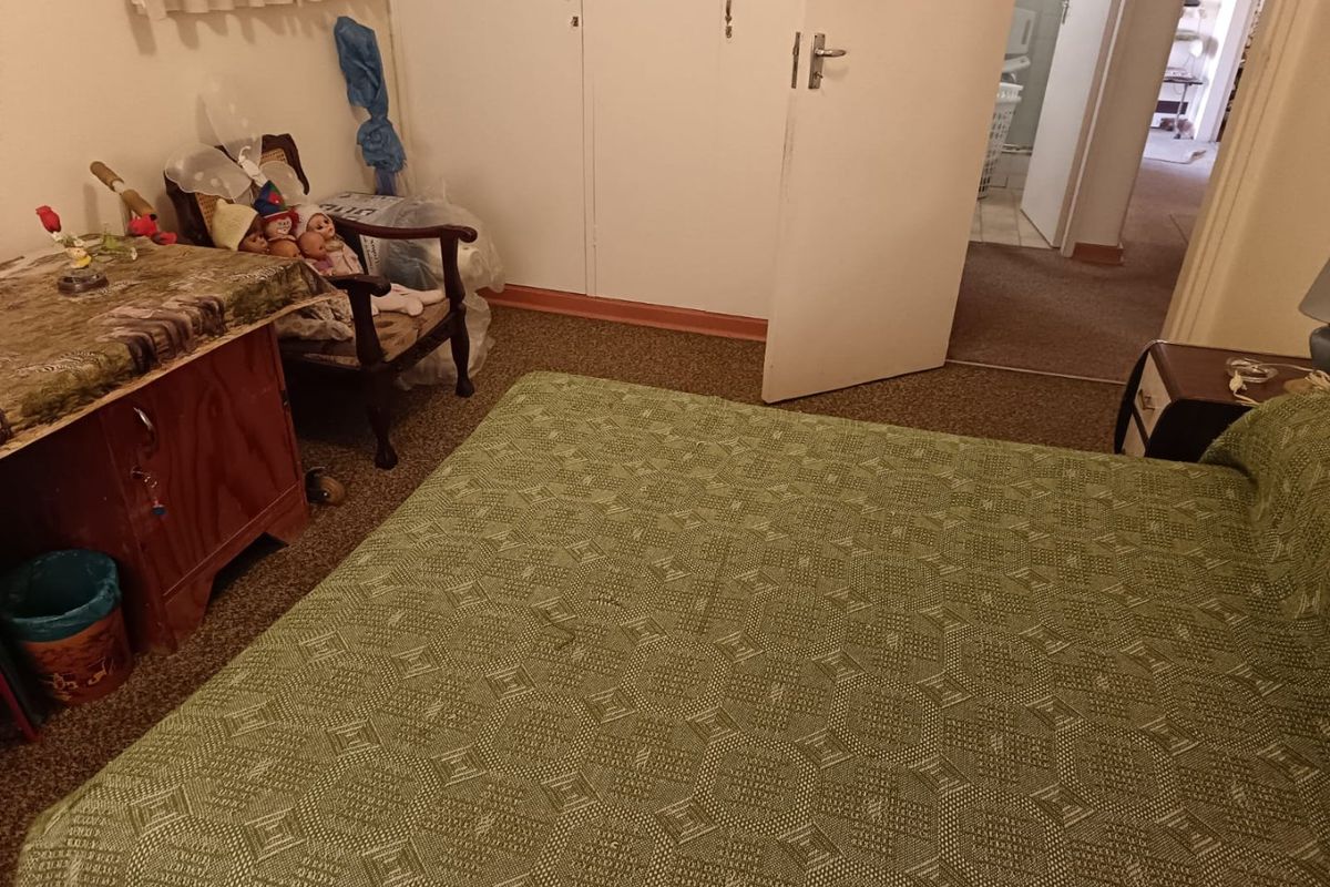 A bedroom featuring built-in cupboards and carpeted flooring, with a view leading into an adjacent hallway.