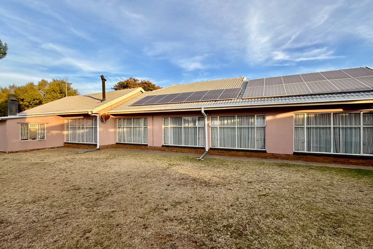 Rear view of the house featuring a tiled roof with installed solar panels, large windows, and a surrounding lawn area.