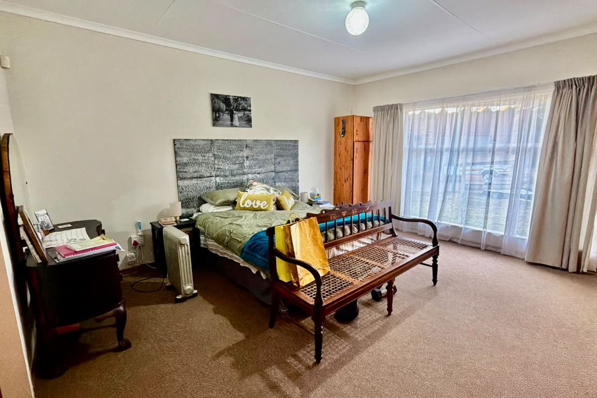 A spacious bedroom featuring neutral wall tones, carpeted flooring, and large windows with curtain tracks, offering a comfortable and functional living space.