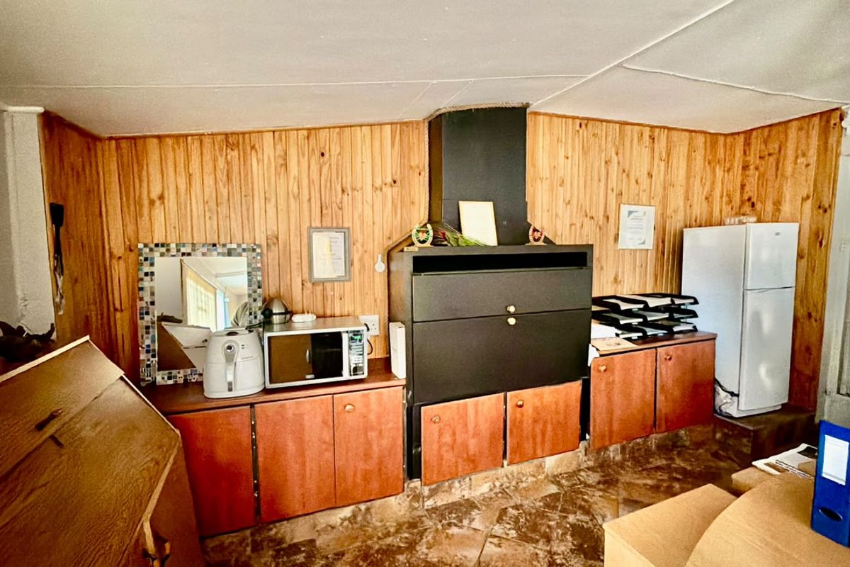 A dated kitchen area featuring timber wall paneling, built-in cabinetry, and a large integrated braai unit with an extractor hood.