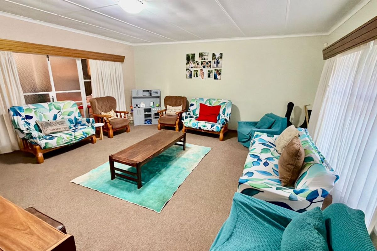 A spacious living room featuring carpeted flooring, large sliding glass doors with curtain pelmets, and neutral wall finishes.