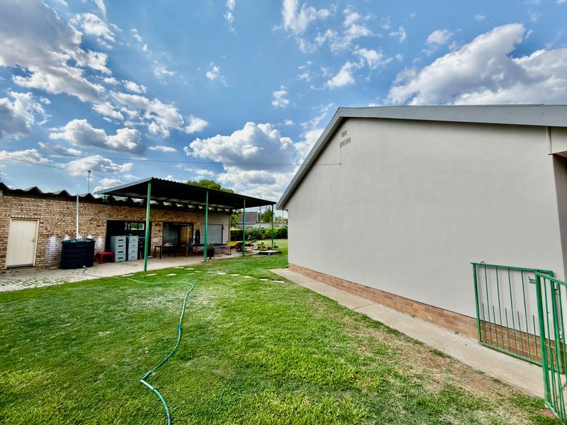 Rear view of the property featuring a lawn, a covered patio area, and a combination of brick and plastered exterior walls.