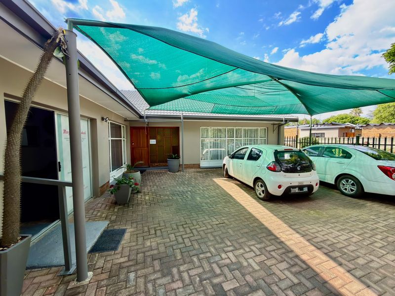Front exterior view featuring a paved driveway, a large green shade sail, and access to the main entrance and sliding glass doors.