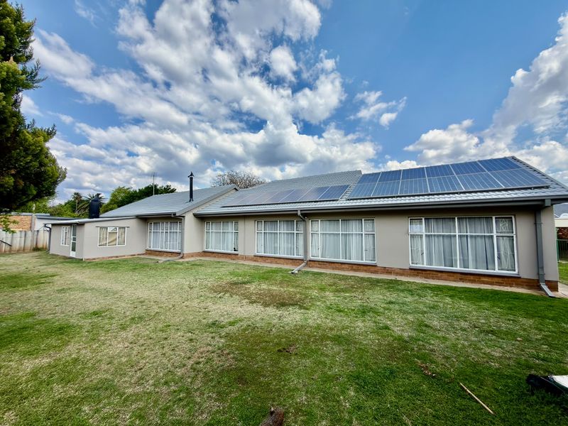 Rear view of the house featuring a well-maintained lawn, large windows, and a roof equipped with solar panels.