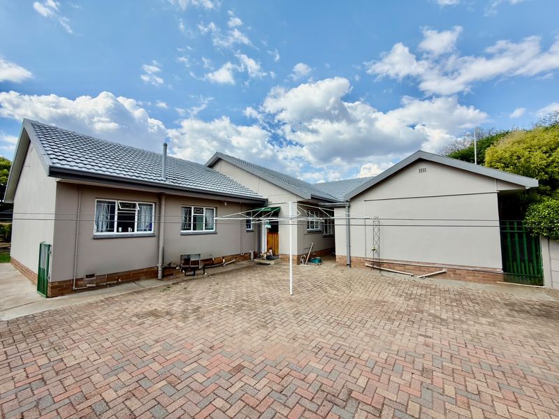 A rear exterior view of the house featuring a paved courtyard, tiled roof, and security-fitted windows.