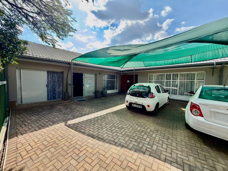 A paved front courtyard area featuring a large shade cloth carport, providing covered parking space with direct access to the main building entrance.