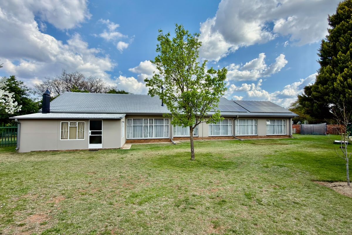 Rear view of a well-maintained single-story house featuring a tiled roof, solar panels, and expansive windows overlooking a spacious lawn.
