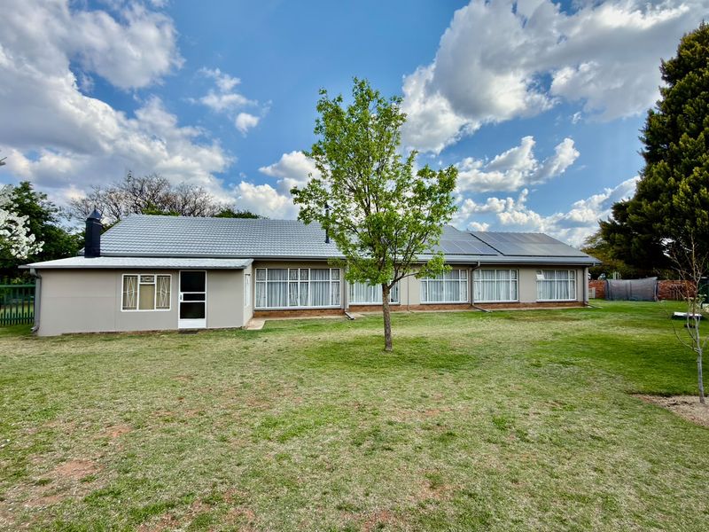 Rear view of a well-maintained single-story house featuring a tiled roof, solar panels, and expansive windows overlooking a spacious lawn.