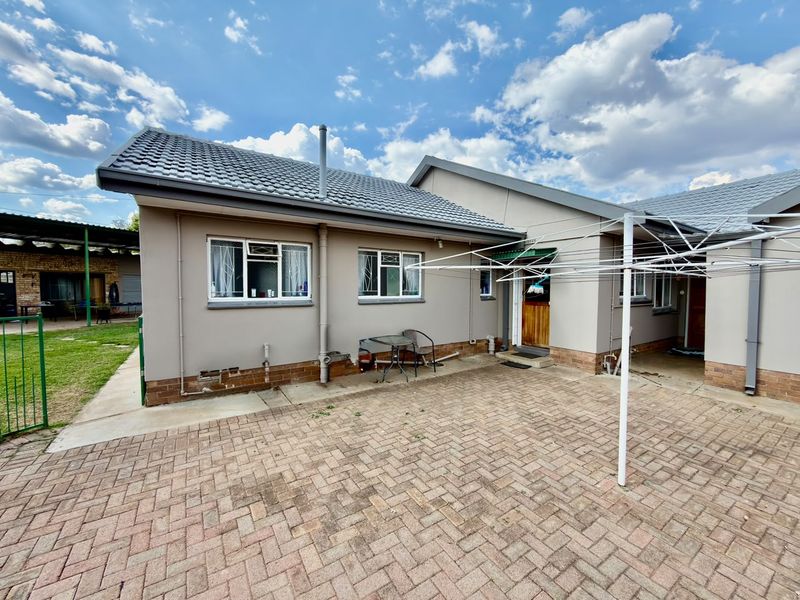 Rear view of the house featuring a paved courtyard, plastered exterior walls, tiled roof, and security-fitted windows.