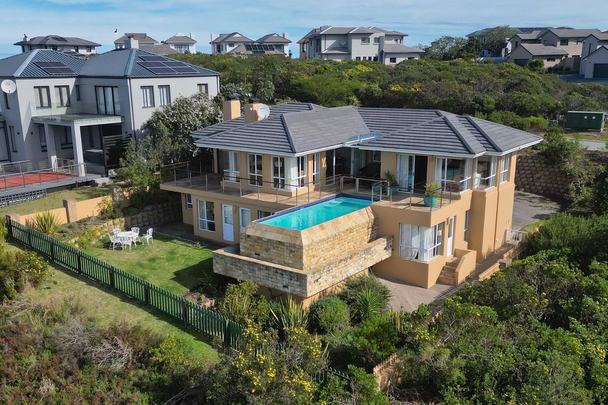 Aerial view of a two-story residential property featuring a raised swimming pool with stone cladding, a spacious balcony, and a landscaped garden.