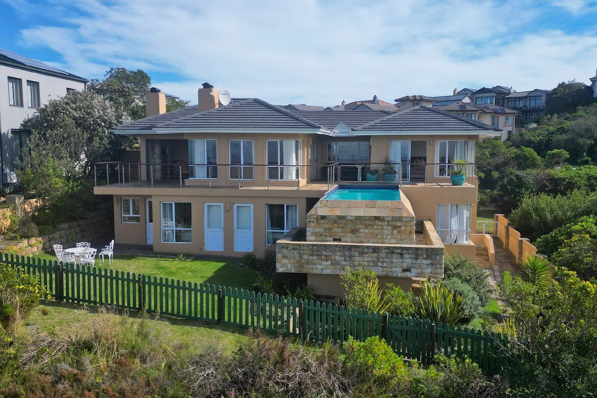 Rear view of a multi-level house featuring a raised swimming pool with stone cladding, a balcony, and a landscaped garden area.