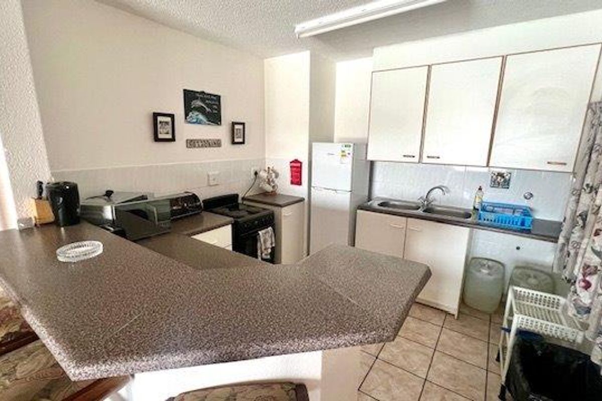 A functional kitchen featuring a breakfast bar, laminate countertops, built-in cabinetry, and a freestanding stove with tiled flooring.