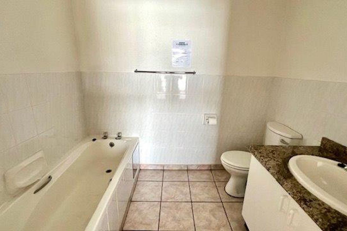 A functional bathroom featuring a bathtub, toilet, and vanity cabinet with a basin, finished with tiled walls and flooring.