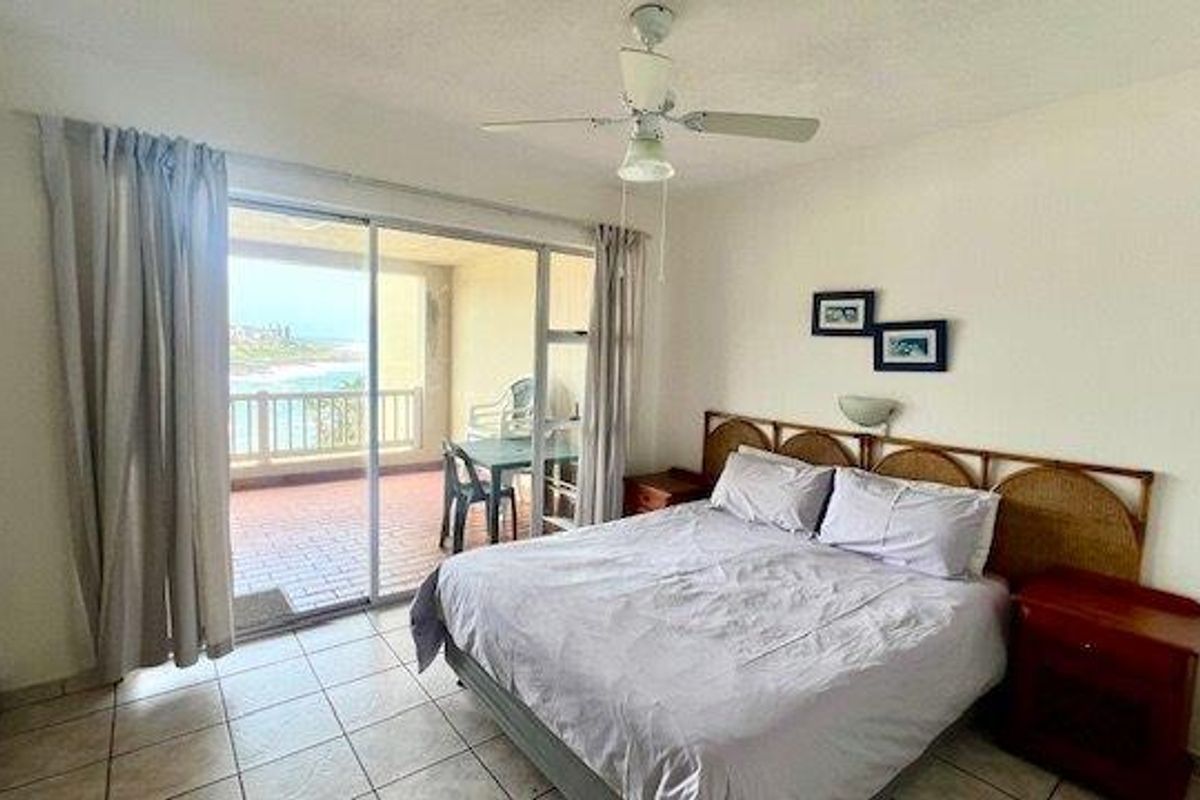 A bedroom featuring tiled flooring, a ceiling fan, and a sliding glass door providing access to a balcony with ocean views.