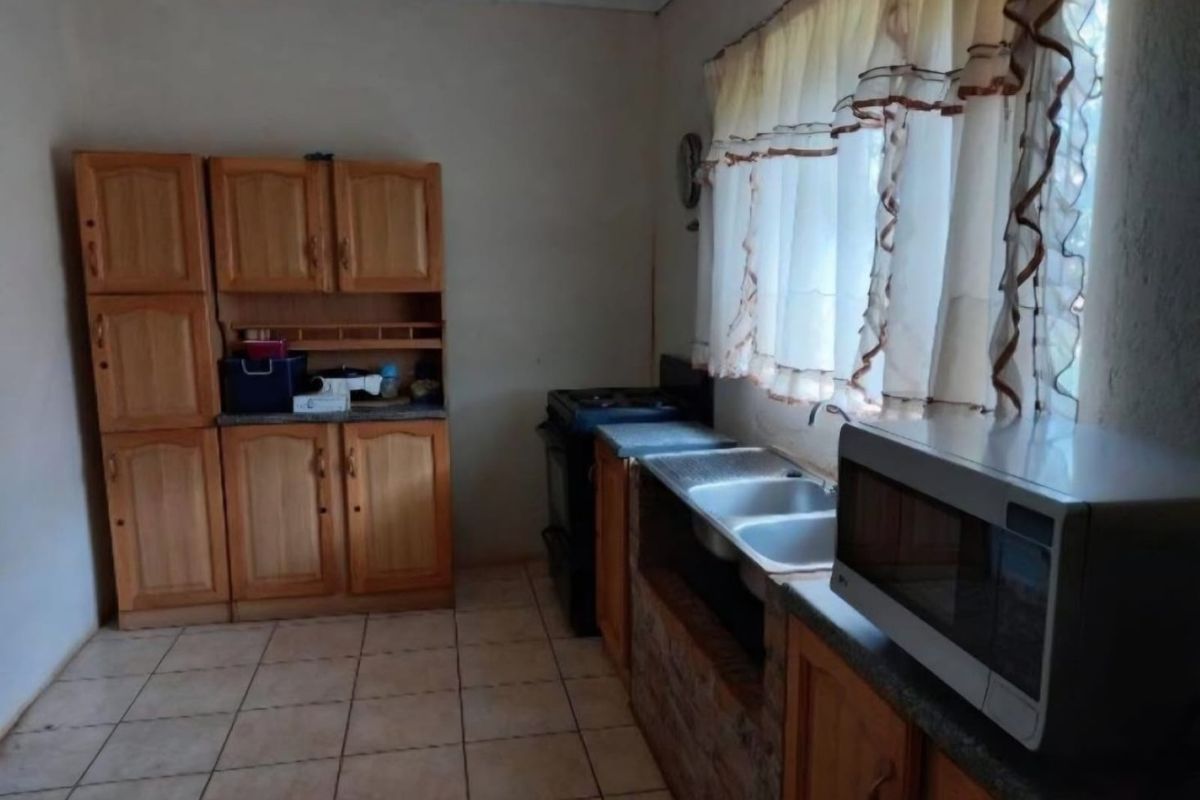 A dated kitchen featuring wooden cabinetry, a double basin sink, and tiled flooring, offering potential for a modern renovation.
