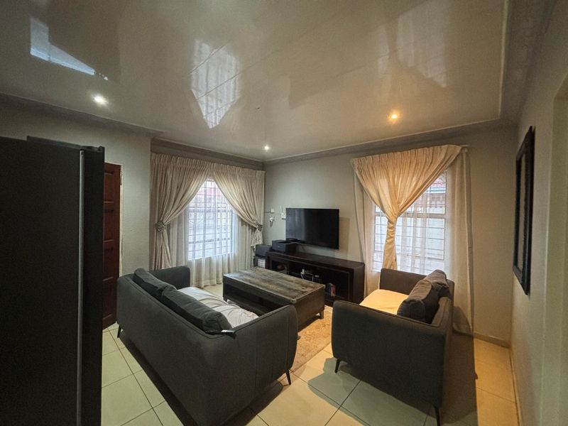 A comfortable living room featuring tiled flooring, recessed downlighting, and a glossy ceiling finish, with security bars installed on the windows.