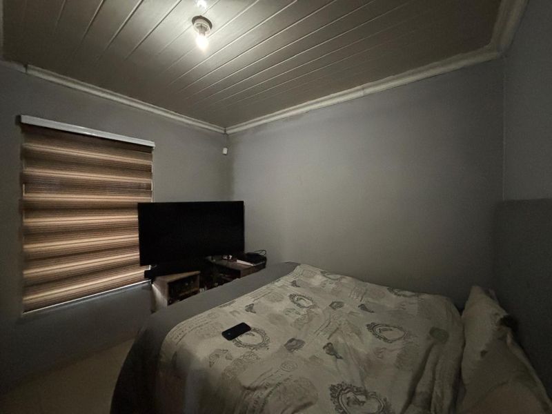 A bedroom featuring a timber-look ceiling, coving, and roller blinds, providing a functional space for rest.