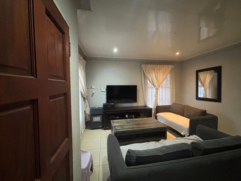 A living room featuring tiled flooring and recessed downlighting, with a glossy ceiling finish and neutral wall tones.