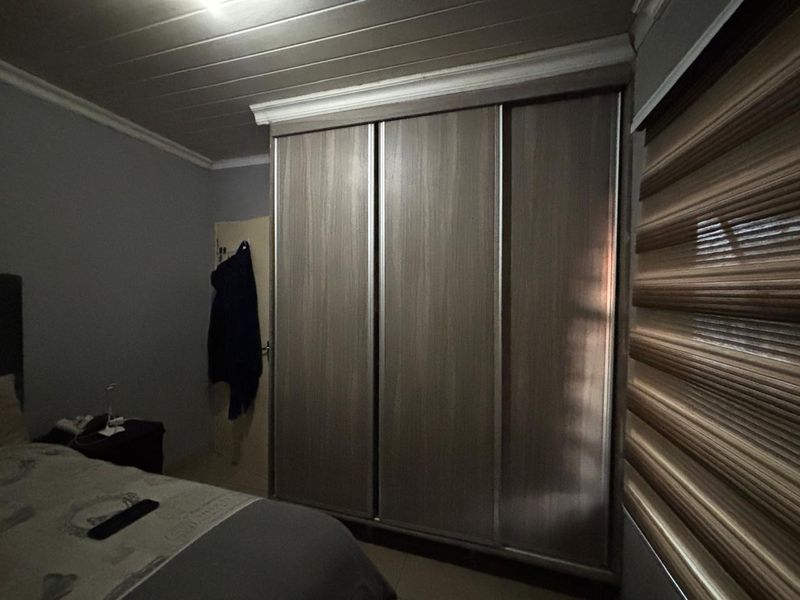 A bedroom featuring a large built-in wardrobe with sliding doors, timber ceiling detailing, and modern roller blinds.