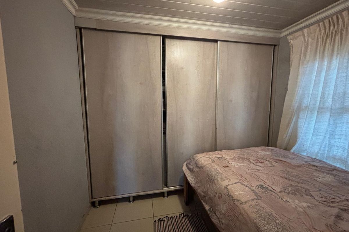 A bedroom featuring built-in sliding door wardrobes, tiled flooring, and a timber panelled ceiling.