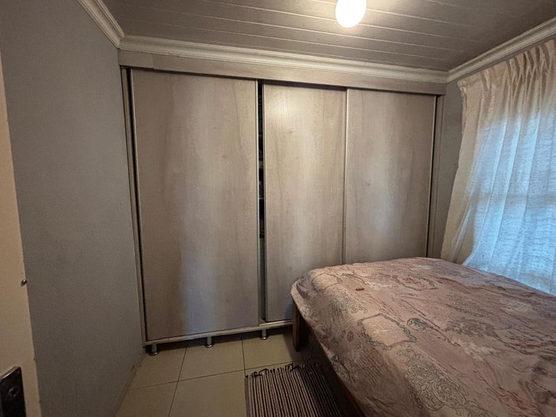 A bedroom featuring built-in sliding door wardrobes, tiled flooring, and a timber panelled ceiling.
