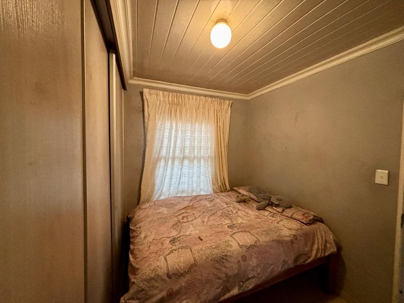 A compact bedroom featuring a built-in wardrobe and a timber tongue and groove ceiling with coving.