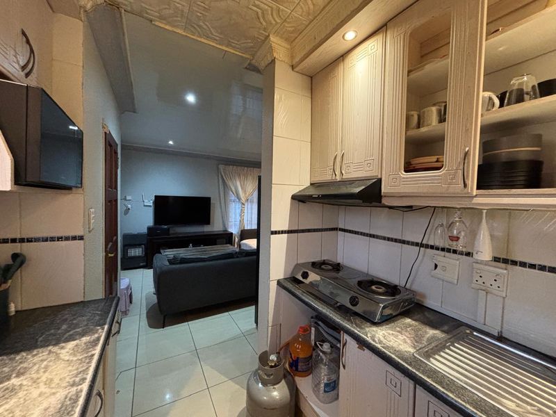 Open plan kitchen area featuring built-in cabinetry, gas hob, and extractor fan, flowing into the adjacent living space with tiled flooring throughout.