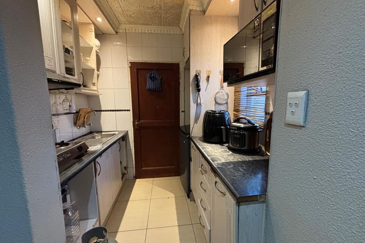 Compact kitchen featuring built-in cabinetry, tiled backsplash, and tiled flooring. The space requires cosmetic updates to modernize the finishes and improve overall functionality.