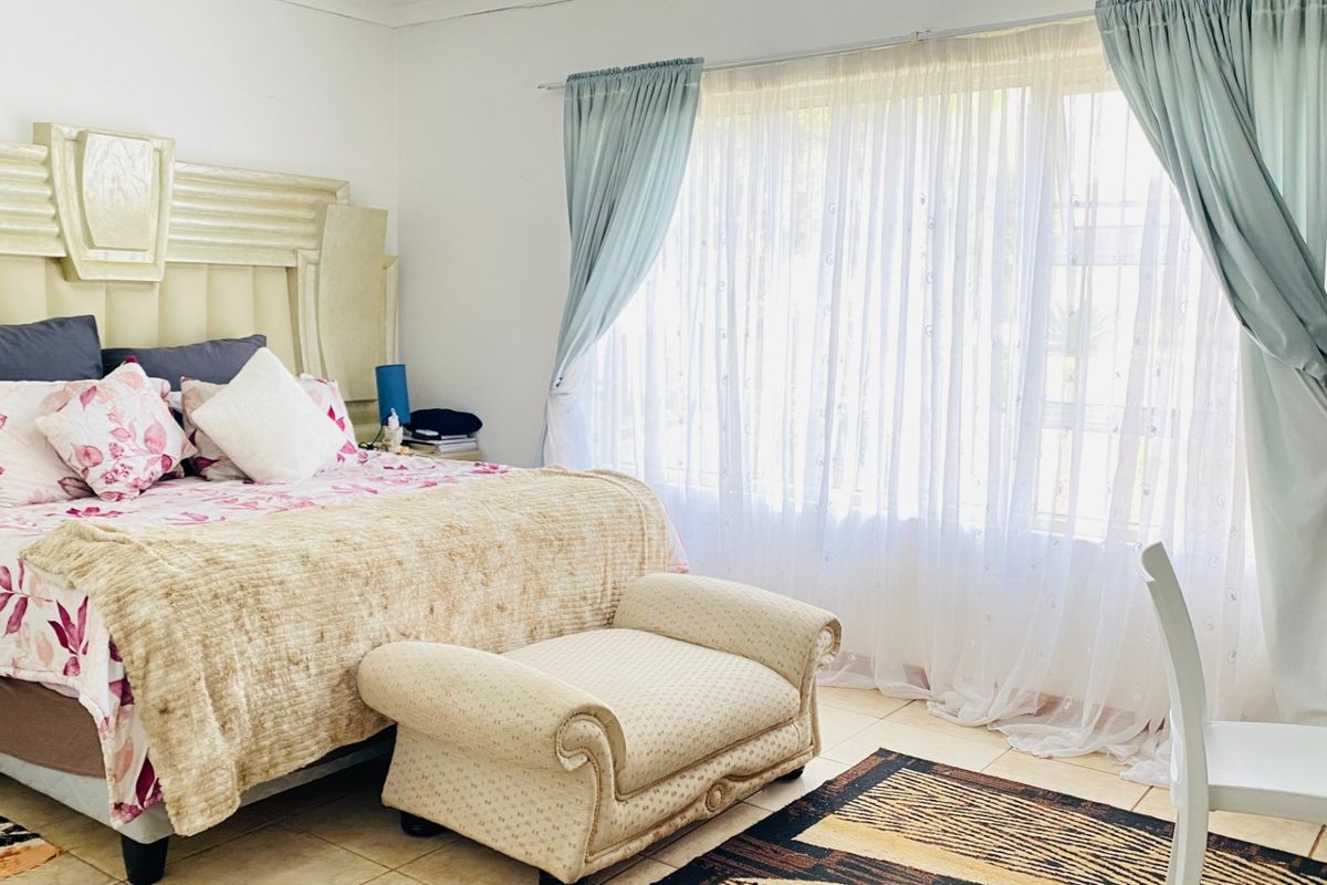 A well-lit bedroom featuring tiled flooring and large windows with installed curtain rails, offering a neutral base for potential interior updates.