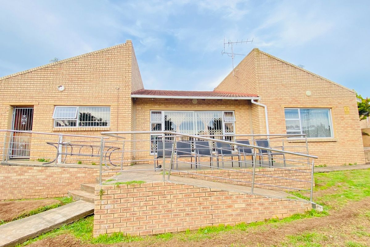 Rear view of a face brick house featuring a concrete access ramp with stainless steel handrails and security gates on windows and doors.