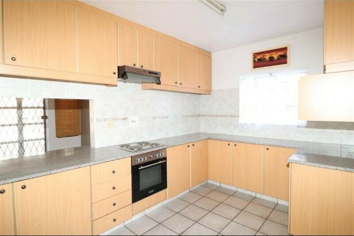 A functional kitchen featuring light wood-finish cabinetry, granite countertops, built-in oven, and hob, complemented by neutral tiled flooring and splashbacks.