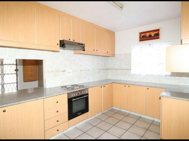 A functional kitchen featuring light wood-finish cabinetry, granite countertops, built-in oven, and hob, complemented by neutral tiled flooring and splashbacks.