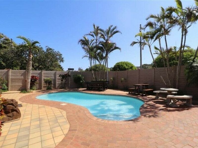 A private outdoor pool area featuring a kidney-shaped swimming pool, paved surround, and secure perimeter walling, ideal for outdoor relaxation.