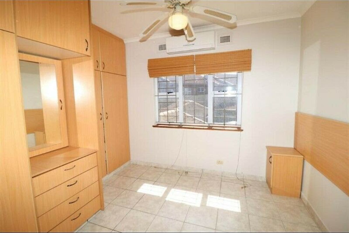 A bedroom featuring built-in wooden cabinetry, tiled flooring, a ceiling fan, and a wall-mounted air conditioning unit.