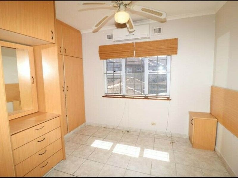 A bedroom featuring built-in wooden cabinetry, tiled flooring, a ceiling fan, and a wall-mounted air conditioning unit.