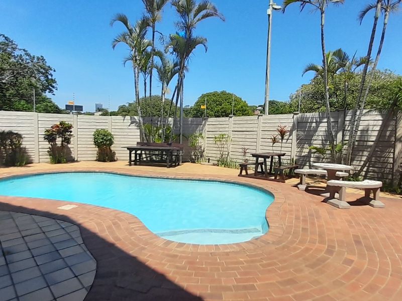 A private outdoor pool area featuring a kidney-shaped swimming pool, brick paving, and a secure perimeter wall with electric fencing.