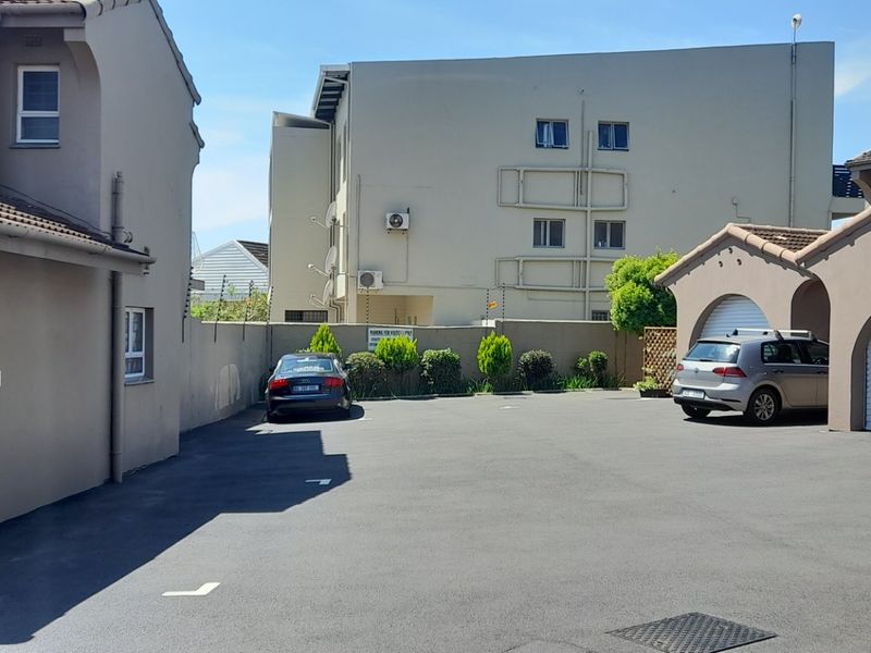 Exterior view of the townhouse complex driveway featuring paved parking areas, secure boundary walls with electric fencing, and multiple roller garage doors.