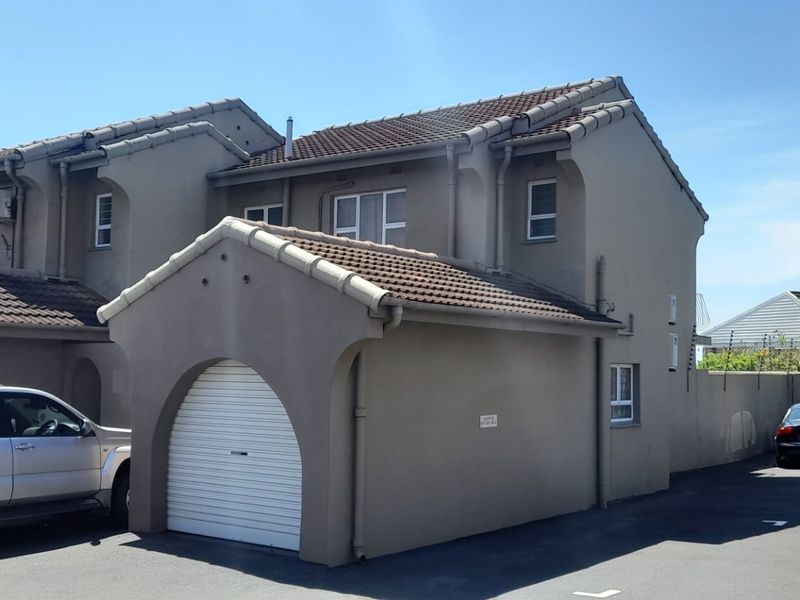 Front elevation of a townhouse featuring a tiled roof, a single roller garage door, and paved driveway access.