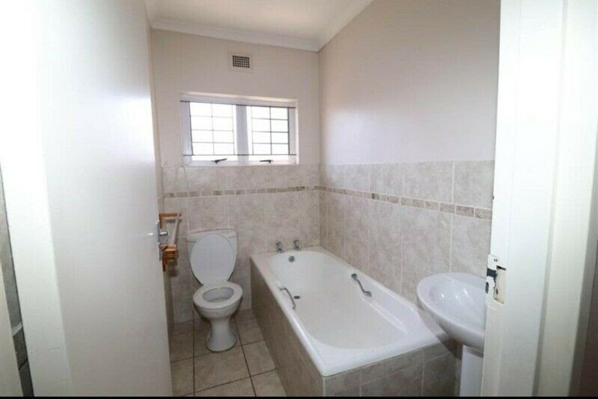 A functional bathroom featuring a pedestal basin, a built-in bathtub, and a toilet, finished with neutral wall and floor tiling.