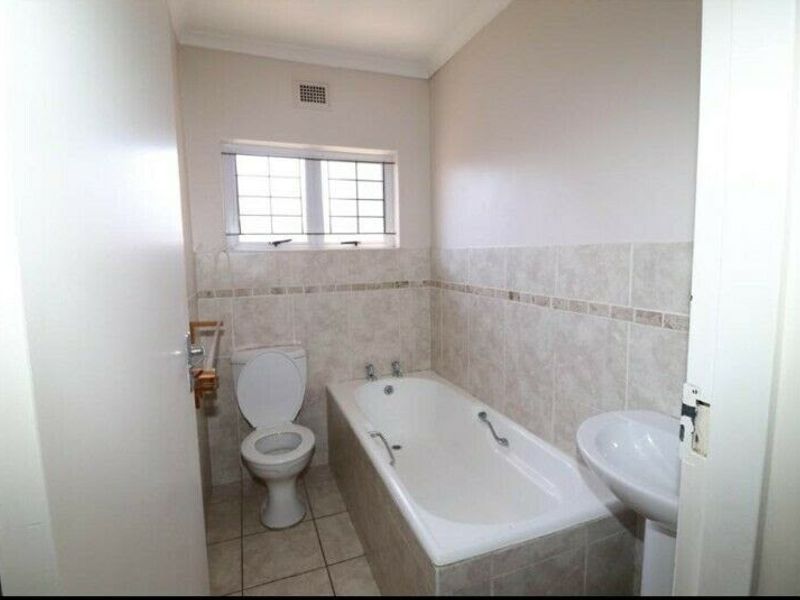 A functional bathroom featuring a pedestal basin, a built-in bathtub, and a toilet, finished with neutral wall and floor tiling.