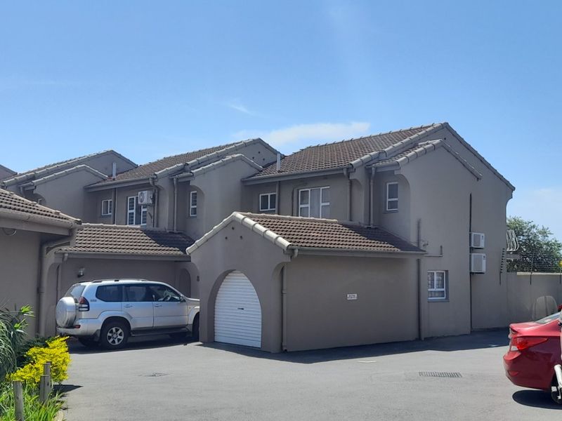Front exterior view of a townhouse complex featuring a paved driveway, tiled roofing, and integrated garage access.
