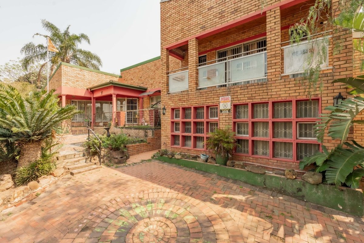 Rear exterior view of a face brick house featuring a paved courtyard, balcony, and established garden elements.