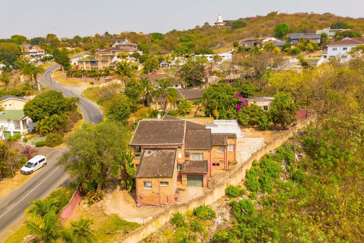Aerial view of a detached brick house with a tiled roof, garage, and boundary wall situated in a residential neighborhood.