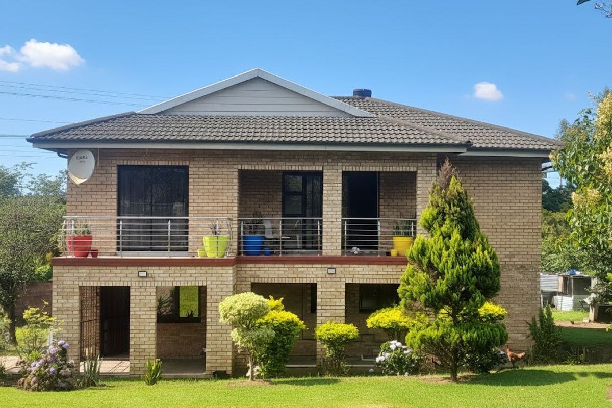 A two-story face brick house featuring an upper-level balcony with stainless steel balustrades and a lower-level covered patio overlooking a landscaped garden.